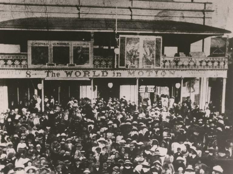 A crowd outside Goulburn's Empire Theatre with a hoarding advertising The World in Motion and posters visible for Les Miserables.