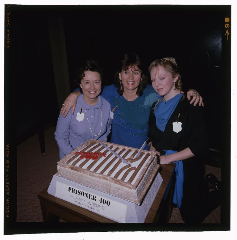 Three members of the cast of Prisoner posing with a decorated cake. A label reads 'Prisoner 400. Reg Grundy's. Network 10 Australia. As seen in Australia'.