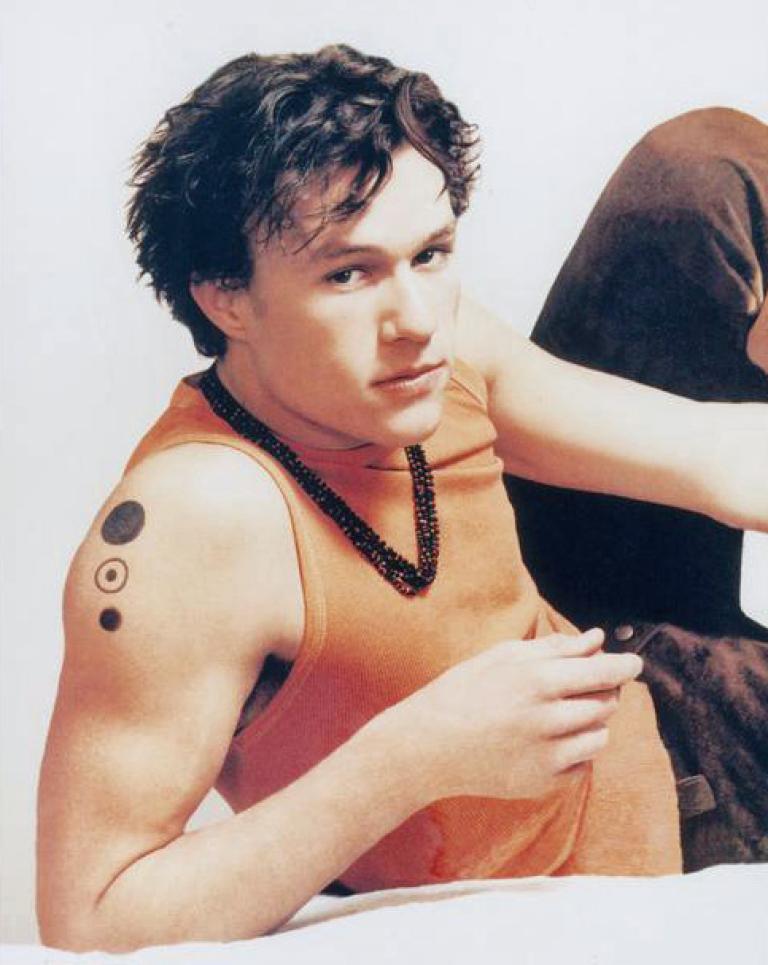 Heath Ledger as Patrick Verona with a seductive look on his face. He is dressed in an orange singlet.