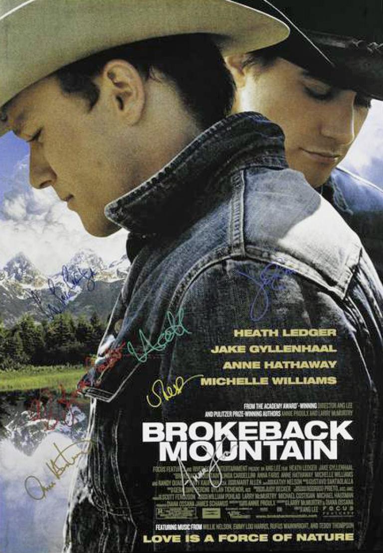 A signed poster for Brokeback Mountain. Heath Ledger and Jake Gyllenhaal are pictured standing in profile. Both men are looking down away from one another. The Rocky Mountains are in the distance.