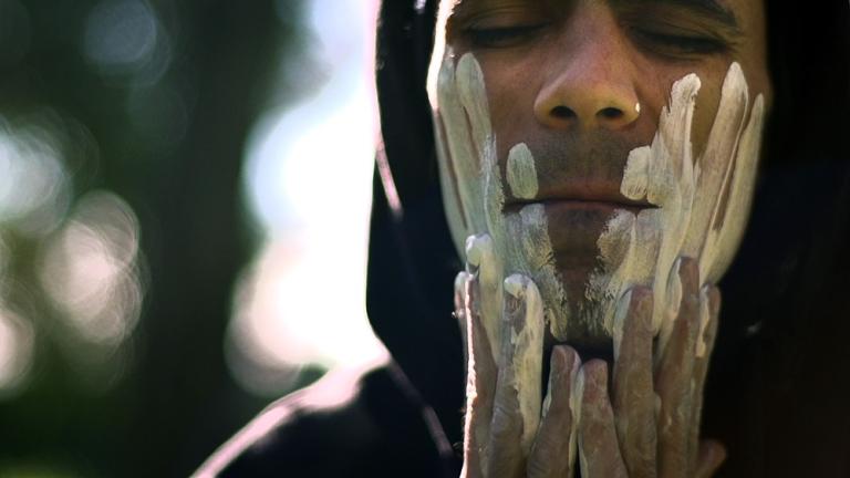 Indigenous man wipes white clay onto his face.