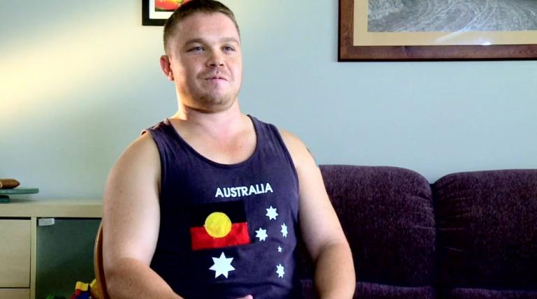 Man wearing a singlet with a print of Indigenous flag inserted where the Union Jack would be on the Australian flag.