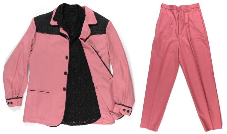 A costume from the film ELVIS consisting of a pink and black jacket, black shirt and pink pants.