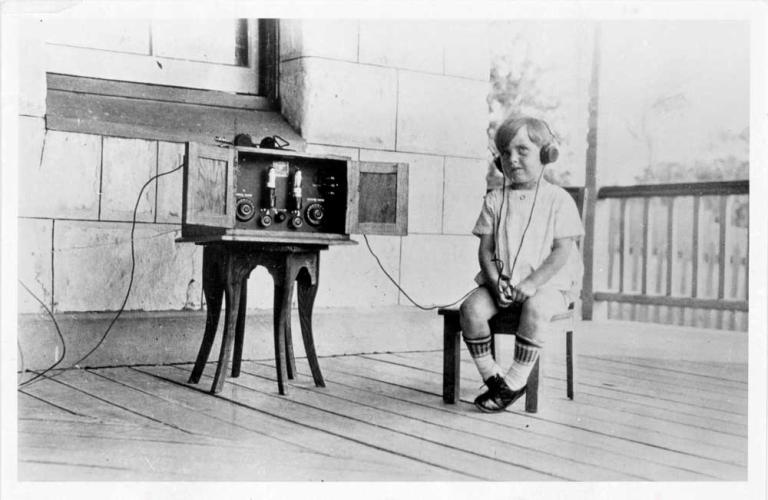 A small child sitting with headphones on and listening to a radio, c1924.