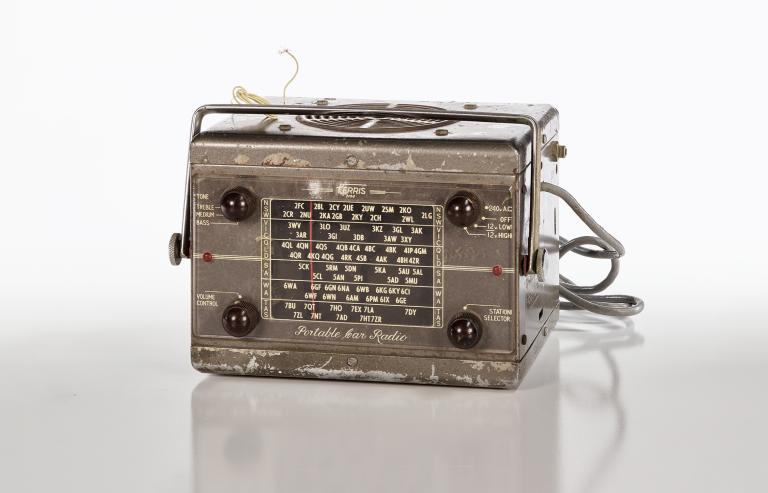 Portable car radio receiver from the 1930s with 4 dials and frequencies listed on the front, a speaker on top and wires coming out of the back.