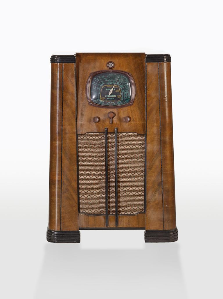 Upright console radio from the 1930s in a wooden housing with a speaker, dial and display on the front.