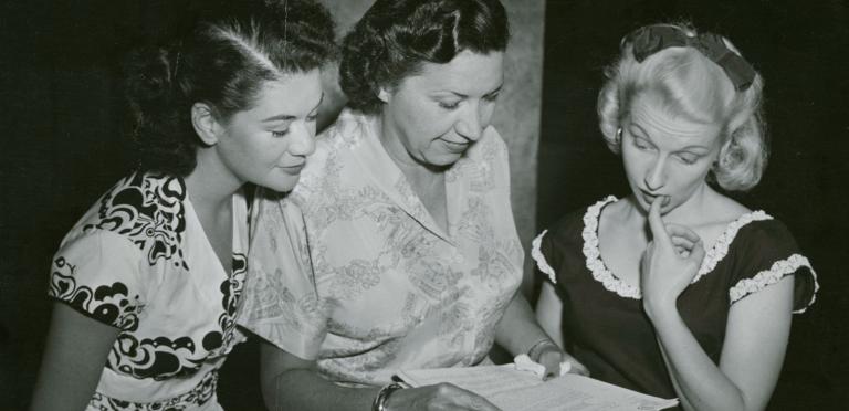 Grace Gibson in the centre of Betty McDowell and Madi Hedd examining a script.