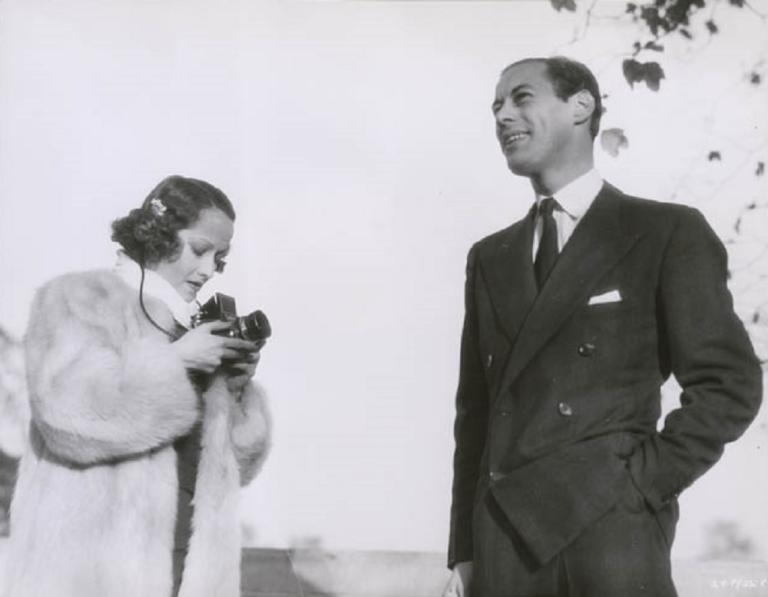 Merle Oberon in a fur coat standing next to Rex Harrison in a smart suit