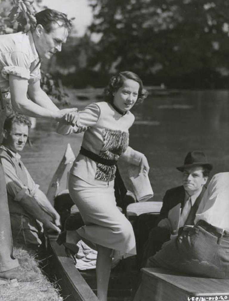 Merle Oberon is helped into a small boat on a river
