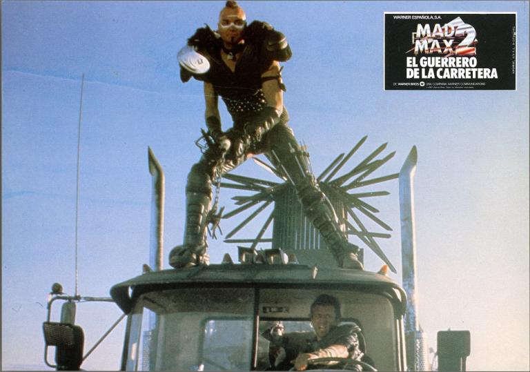 Mad Max 2 lobby card showing Wez (Vernon Wells) riding on top of a truck cabin