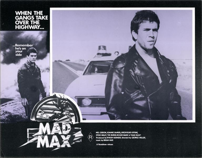 Lobby card for Max Max shows Max (Mel Gibson) standing on a highway with a police car behind him.