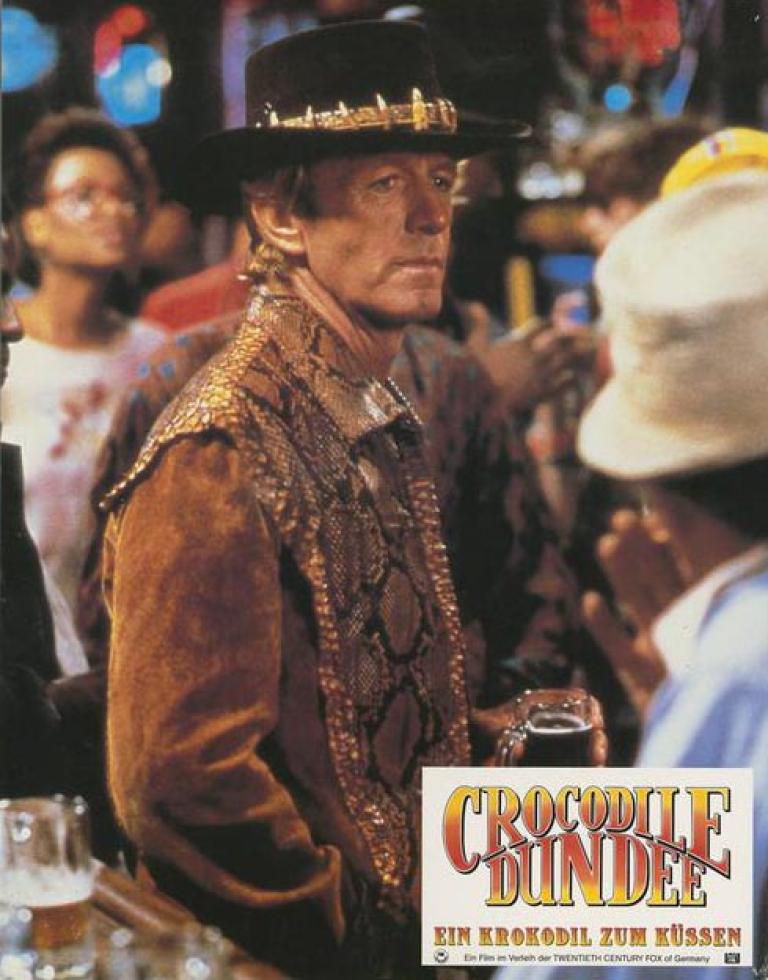 Lobby card depicting Paul Hogan as Mick Dundee standing in a bar in New York City by himself
