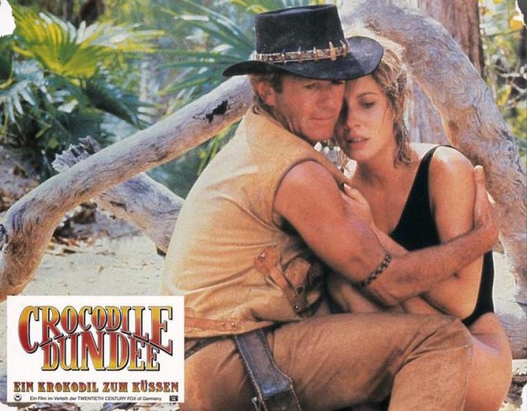 Lobby card depicting Mick Dundee in a protective embrace with Sue Charlton after she got attacked by a crocodile
