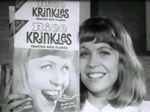 Jacki Weaver, smiling and holding a box of 'Rice Krinkles', featuring her face on the front. In the box, Jacqui is seen eating the product.