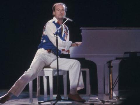 Peter Allen is singing at a grand piano.