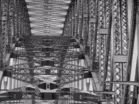 Black and white still of the view between the top and bottom of the arches of the Sydney Harbour Bridge. 