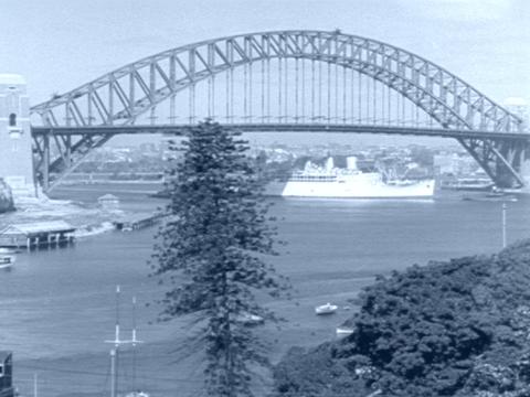 Blue tinted back and white image of Sydney Harbour Bridge with a large cruise ship passing underneath in the 1930s