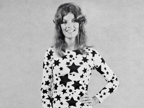 Upper body shot of singer/songwriter Alison McCallum, smiling at camera with her hand on hip. Wearing a fitted dress covered in stars.