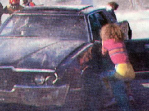 A black car with smoke coming out of it and a girl (Nicole Kidman) kneeling down looking into one of the car windows.