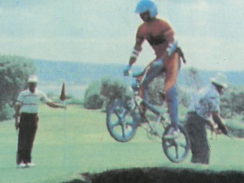 Teen on a BMX bike going over a jump on a golf course