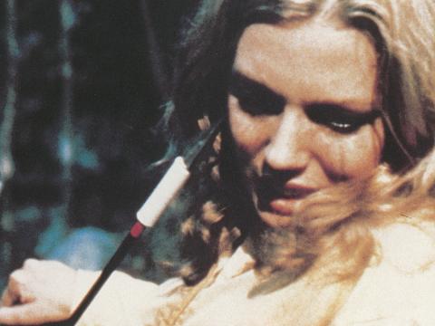 Close up of Rita Daniels (played by Lynda Stoner) in a scene from Turkey Shoot. Someone off camera is holding an arrow up to her face in a threatening way. 