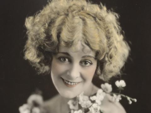 A hand-coloured publicity portrait of actor Vera James. Her face is bordered by cherry blossoms.