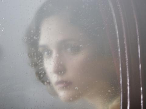 Rose Byrne as Iris in The Tender Hook, looks out a window that is fogged over and covered in raindrops.