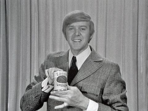 Entertainer Barry Crocker, circa 1969 looking at camera and holding a can of Lassie brand dog food.