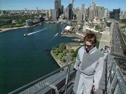 A woman wearing grey overalls climbs to the top of the Sydney Harbour Bridge with Bridge Climb.