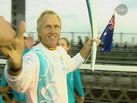 Golfer Greg Norman carries the Olympic torch and a small Australian flag across the Sydney Harbour Bridge in 2000