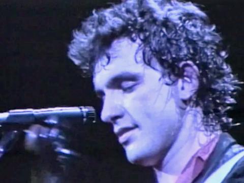 Close up of Cold Chisel band member Ian Moss in profile, facing a microphone with his eyes closed.