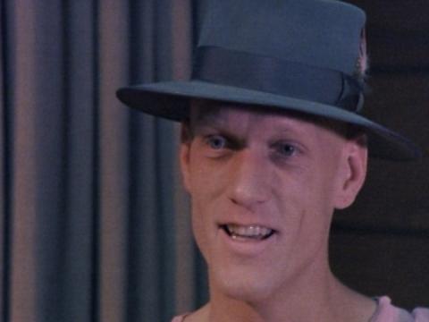 Close up of singer Peter Garrett wearing a grey hat and talking to camera. 