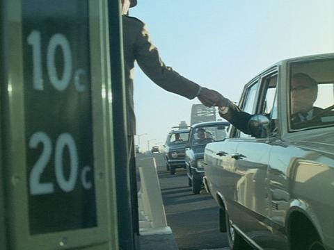 A toll collector on the Sydney Harbour Bridge reaches out to get the toll from a person in a car. There is a sign with lights for 10 cents and 20 cents.