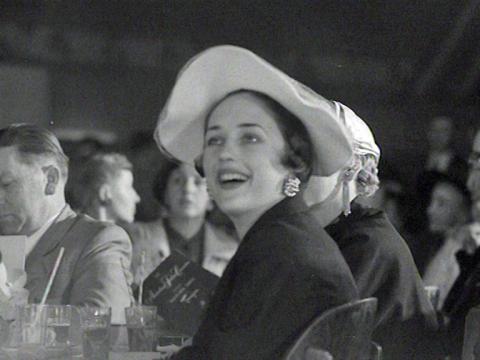 A woman wearing a hat is looking up at something with a look of delight.
