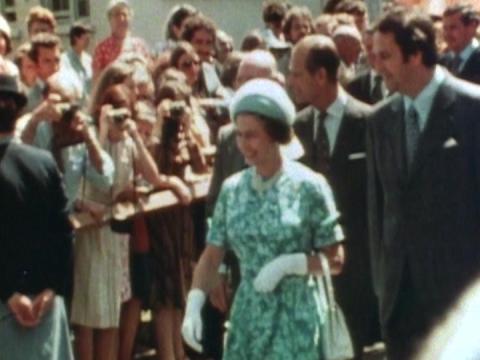 Queen Elizabeth II walking through a crowd of people with cameras, Prince Phillip behind her