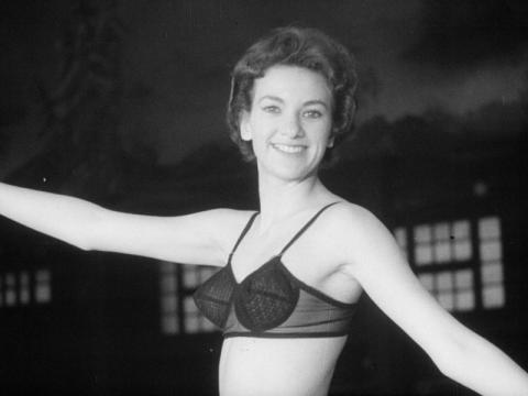 A woman poses with her arms outstretched. She is wearing only a bra.