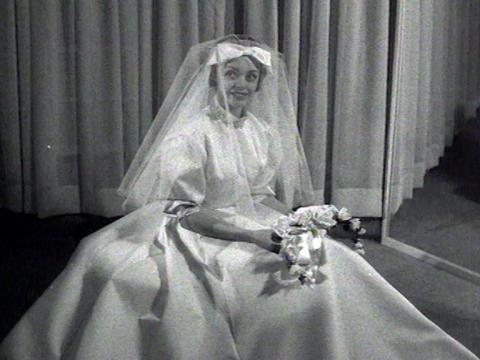 Woman wears a volumous wedding gown complete with veil and bow.