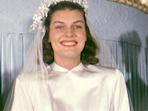 A woman smiles at the camera. She is wearing a wedding dress and veil.