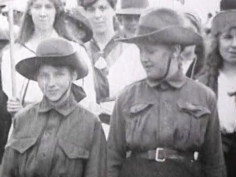 Two boys in soldiers' uniforms at an Anzac Day stand with a crowd of people at the first Anzac Day commemoration