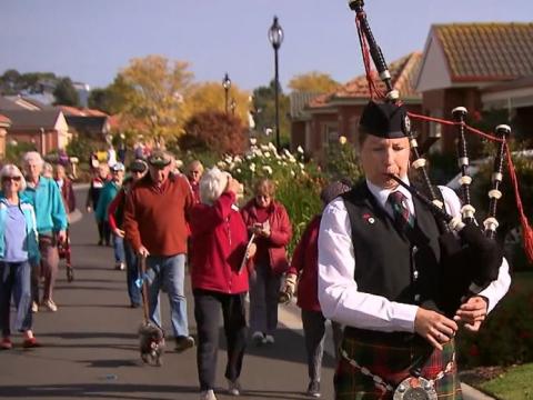 A bagpipe player on a suburban street followed by a crowd