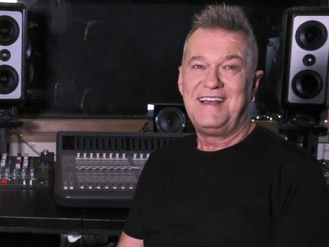 Singer Jimmy Barnes pictured from the chest up, in a black t-shirt and sitting in front of a mixing deck in a recording studio. 