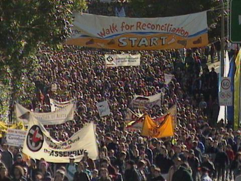 Thousands of people marching in the street on the Walk for Reconciliation on 28 May 2000 in Sydney. Many are carrying flags and banners to show their support.  