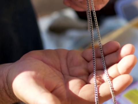 Close up of a man's hand holding two chain link style necklaces