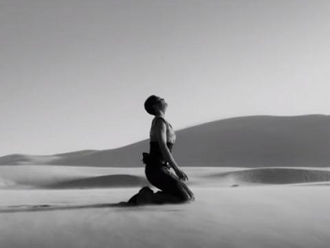 Black and white image showing a women kneeling in the desert.