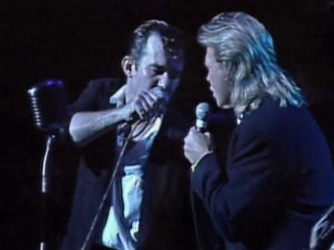 Jimmy Barnes and John Farnham on stage together, both are holding microphones and are turned towards each other