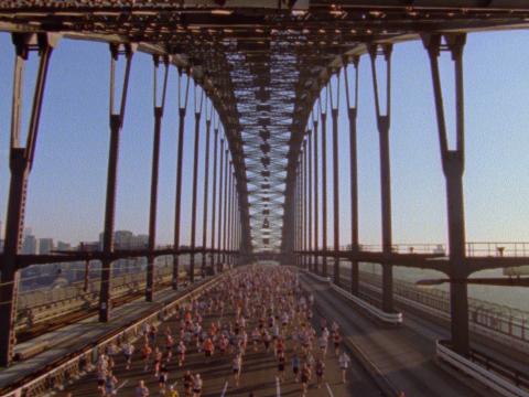 A view of the Sydney Harbour Bridge from above with marathon runners running across the roadway.