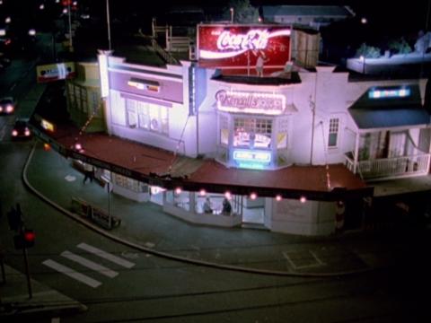 An overhead shot of shops on a street corner topped by a Coca Cola sign, in a scene from Strictly Ballroom