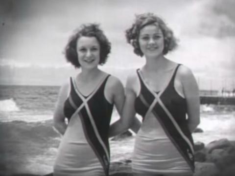 Black and white image of two young ladies in bathing suits smiling at the camera at Bondi beach, circa 1929