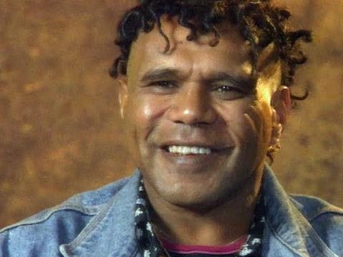 Close up of Indigenous singer-songwriter Archie Roach. He's wearing a denim jacket and smiling at the camera.