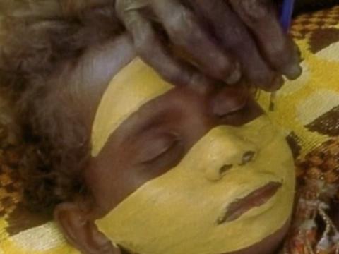 Close up of a child having his face painted in wide yellow bands